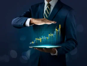 A businessman in a suit holds a tablet displaying a glowing upward stock graph, symbolizing financial growth and investment success.