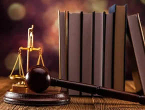 A wooden gavel resting on a small stack of books, accompanied by a flickering candle, set against a dark backdrop with soft lighting to highlight the objects in the scene.
