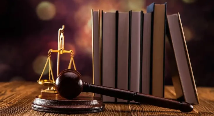 A wooden gavel resting on a small stack of books, accompanied by a flickering candle, set against a dark backdrop with soft lighting to highlight the objects in the scene.