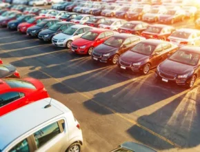 Aerial view of a crowded parking lot filled with rows of colorful cars, including red, black, and silver vehicles, casting long shadows.