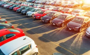 Aerial view of a crowded parking lot filled with rows of colorful cars, including red, black, and silver vehicles, casting long shadows.