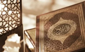 A beautifully ornate Quran on a table, illuminated by soft light from a decorative lantern in the background.
