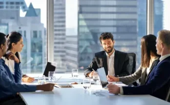 A diverse group of professionals in business attire engages in a meeting around a modern conference table, with a city skyline in the background.