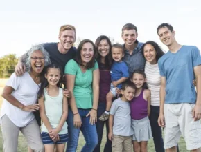 A diverse group of family members poses together outdoors, showcasing smiles and a range of casual summer outfits in a sunny setting.