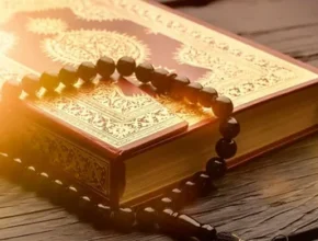 The Quran book rests on a wooden surface, accompanied by a black prayer bead necklace, creating a serene atmosphere.