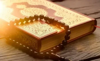 The Quran book rests on a wooden surface, accompanied by a black prayer bead necklace, creating a serene atmosphere.