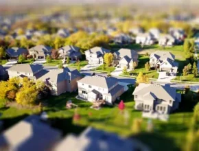 Aerial view of a suburban neighborhood with neatly arranged houses, green lawns, and trees in autumn colors.