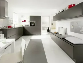 Modern kitchen with sleek dark cabinets, a white dining table, and minimalist decor, featuring a cozy seating area and vibrant red accents.