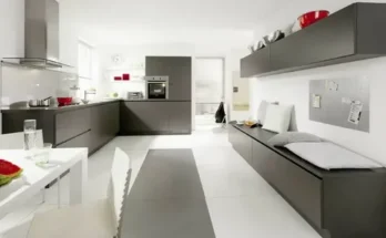 Modern kitchen with sleek dark cabinets, a white dining table, and minimalist decor, featuring a cozy seating area and vibrant red accents.