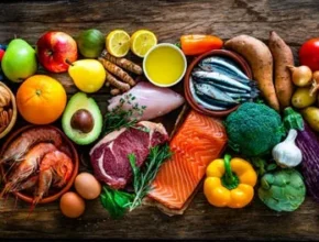 A vibrant assortment of fresh fruits, vegetables, seafood, meat, and nuts arranged on a wooden surface, showcasing healthy food choices.