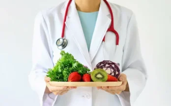 A healthcare professional in a white coat holds a wooden plate filled with fresh fruits and vegetables, symbolizing healthy eating.