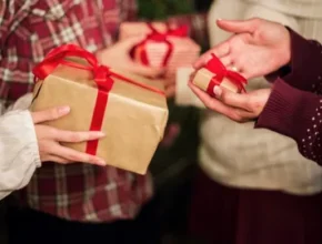 People exchanging gifts during a festive gathering, with wrapped presents featuring decorative bows. Warm holiday atmosphere.