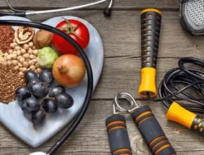 A heart-shaped plate filled with healthy foods, surrounded by a stethoscope, workout grips, and running shoes on a wooden surface.