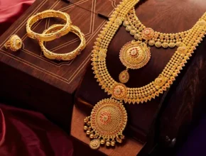 Elegant gold jewelry set featuring a detailed necklace, matching earrings, and bangles, displayed on a wooden box with rich fabric.