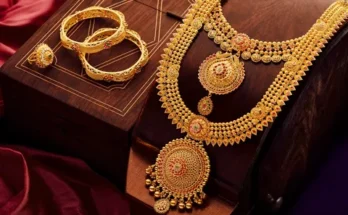 Elegant gold jewelry set featuring a detailed necklace, matching earrings, and bangles, displayed on a wooden box with rich fabric.