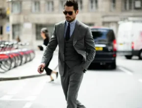 A well-dressed individual in a tailored gray suit walks confidently along a bustling city street, surrounded by bikes and vehicles.