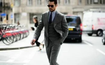 A well-dressed individual in a tailored gray suit walks confidently along a bustling city street, surrounded by bikes and vehicles.
