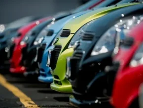 A row of parked cars in vibrant colors, prominently showcasing their hoods and grilles in a blurred parking lot background.