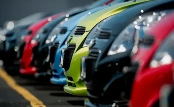 A row of parked cars in vibrant colors, prominently showcasing their hoods and grilles in a blurred parking lot background.