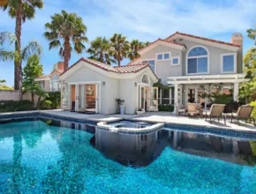A luxurious home with a sparkling pool, surrounded by palm trees, featuring a spa and a spacious patio for relaxation.