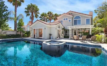 A luxurious home with a sparkling pool, surrounded by palm trees, featuring a spa and a spacious patio for relaxation.