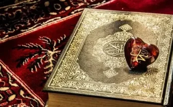 A beautifully quran book sits on a rich, patterned rug, topped with a glossy red heart-shaped object engraved with the word Muhammad.