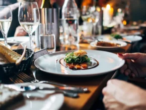 An elegantly set dining table with sparkling wine, water, and a gourmet plate of salmon topped with greens, alongside fresh bread.