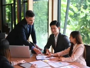 A group of business professionals engaged in a meeting, analyzing documents and discussing strategies in a well-lit conference room.