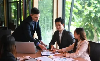 A group of business professionals engaged in a meeting, analyzing documents and discussing strategies in a well-lit conference room.