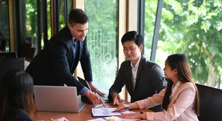 A group of business professionals engaged in a meeting, analyzing documents and discussing strategies in a well-lit conference room.