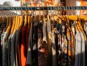 A close-up of a rack of colorful, patterned clothing on wooden hangers, with sunlight casting shadows on the fabrics.
