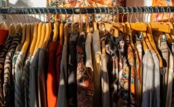 A close-up of a rack of colorful, patterned clothing on wooden hangers, with sunlight casting shadows on the fabrics.