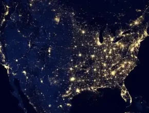 A nighttime satellite image of the United States, highlighting major cities and highways illuminated by lights against a dark background.