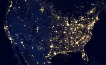 A nighttime satellite image of the United States, highlighting major cities and highways illuminated by lights against a dark background.