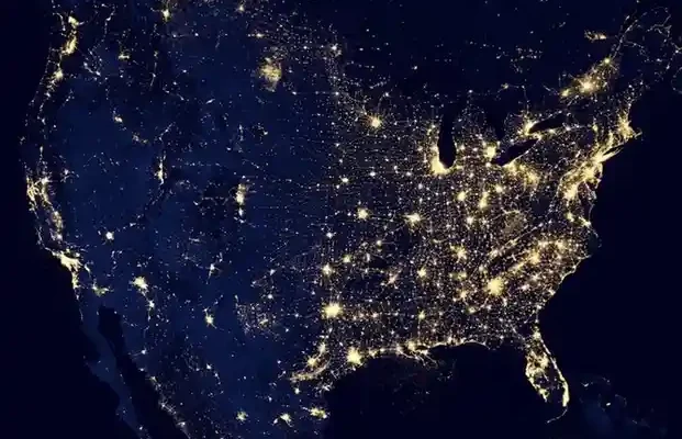 A nighttime satellite image of the United States, highlighting major cities and highways illuminated by lights against a dark background.