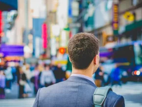 A suited man stands in Times Square, looking toward a bustling crowd and vibrant advertisements, capturing the city's energetic atmosphere.