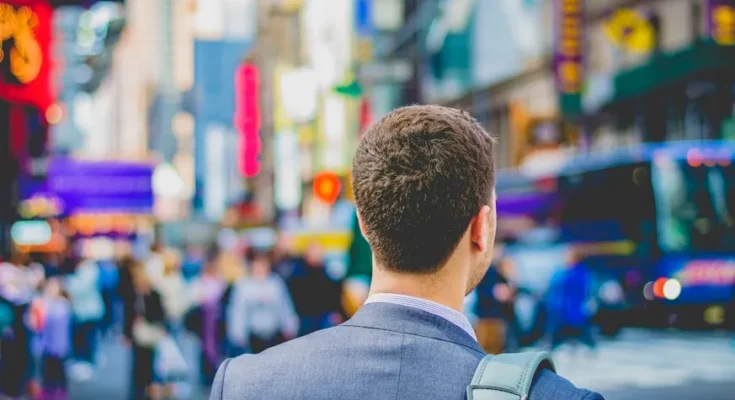 A suited man stands in Times Square, looking toward a bustling crowd and vibrant advertisements, capturing the city's energetic atmosphere.