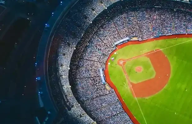 Aerial view of a packed baseball stadium, showcasing the vibrant green field and bustling crowd surrounding the diamond.