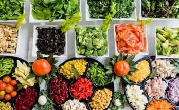 A vibrant array of fresh vegetables and toppings neatly arranged in bowls, featuring greens, peppers, olives, and fruits.