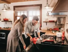 A couple in a cozy kitchen, preparing a meal together with a red pot on the stove, surrounded by fresh ingredients and kitchenware.