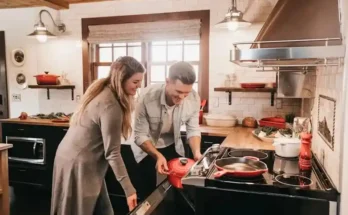 A couple in a cozy kitchen, preparing a meal together with a red pot on the stove, surrounded by fresh ingredients and kitchenware.