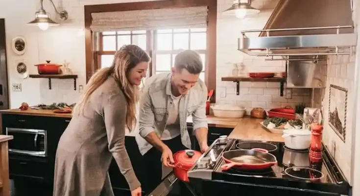 A couple in a cozy kitchen, preparing a meal together with a red pot on the stove, surrounded by fresh ingredients and kitchenware.