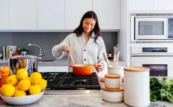 A person stirs a pot on a modern stove in a bright kitchen, surrounded by fresh lemons and neatly arranged kitchenware.