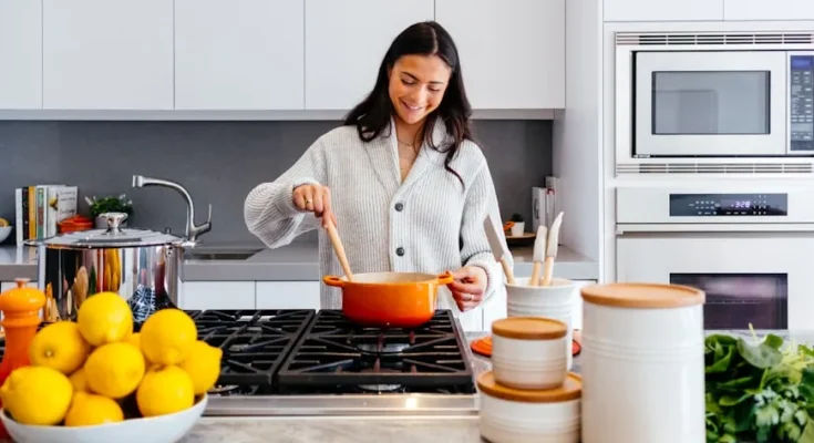 A person stirs a pot on a modern stove in a bright kitchen, surrounded by fresh lemons and neatly arranged kitchenware.