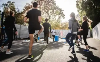 A group of individuals jogs together outdoors, with trees and sunlight in the background, engaged in a fitness workout.
