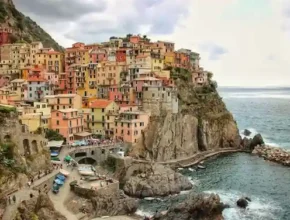 Colorful cliffside houses of Manarola, Italy, overlooking the blue sea, with rocky shores and a scenic harbor below.