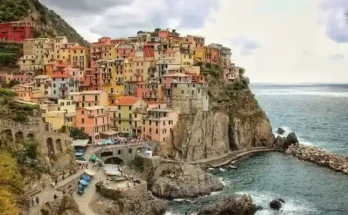 Colorful cliffside houses of Manarola, Italy, overlooking the blue sea, with rocky shores and a scenic harbor below.