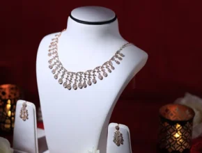 Elegant rose gold necklace displayed on a bust, accompanied by matching earrings, set against a festive red backdrop with candles.