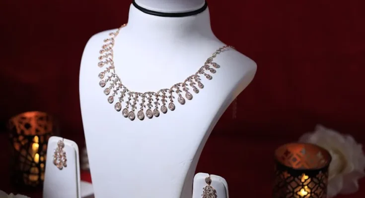 Elegant rose gold necklace displayed on a bust, accompanied by matching earrings, set against a festive red backdrop with candles.