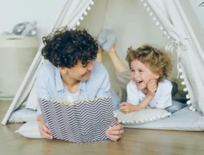 A cozy scene of a parent reading a book inside a tent-like structure to a child, surrounded by soft cushions and playful decor.